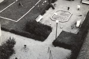 Översikt över Kronhusparken där två pojkar spelar badminton och en mamma med barn står vid en sandlåda.